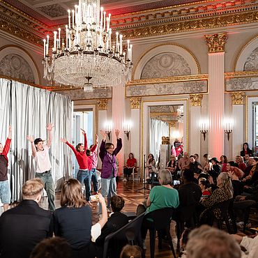 People watch dancers in front of a silver curtain