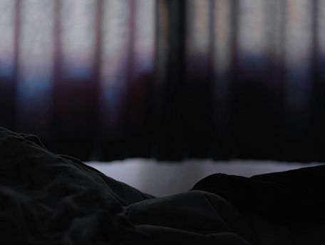 Foto: Perspektive eines Menschen der im Bett liegt und auf ein Fenster mit Vorh&auml;ngen blickt