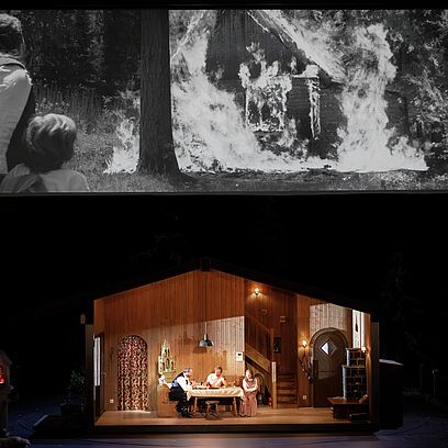 Hunding, Siegmund, and Sieglinde are in a hut. On a screen above the stage, Wotan and the young Siegmund are seen in a flashback in front of a burning hut.