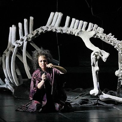 Szene Parsifal: Eine Frau sitzt unter dem gro&szlig;en Skelett eines Tieres