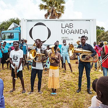 Menschen mit Bla&szlig;instrumenten stehen vor einem Lastwagen mit dem Schriftzug Lab Uganda