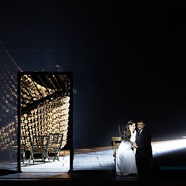 Szenenbild La traviata: Ein Mann und eine Frau sitzen neben einem gro&szlig;en abgest&uuml;rzten Kronleuchter 