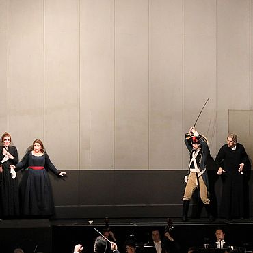 Szenenbild Il barbiere di Siviglia: Eine Gruppe von M&auml;nnern will zwei Frauen und eine  Mann angreifen