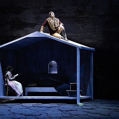 Szenenbild Faust: Marguerite sitzt in ihrem Haus, Faust steht auf dem Dach