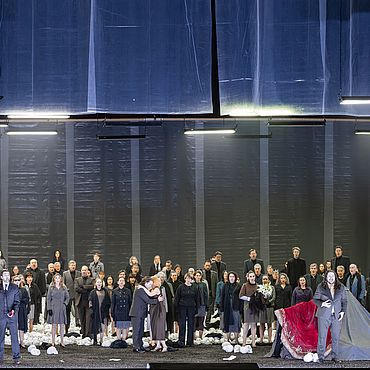 Szenenbild Macbeth: Ein Paar umarmt sich, eine Gruppe von Menschen steht hinter ihnen