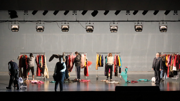 Szene aus Ariadne auf Naxos: Volle Kleiderst&auml;nder auf der B&uuml;hne, Menschen w&uuml;hlen durch die Kleidung